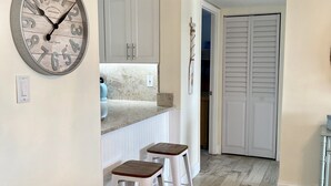 A kitchen with white cabinets, a clock, and two stools. - Beachfront (Cape Canaveral)