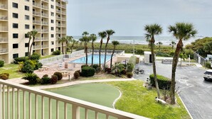 A pool area with a view of the ocean, surrounded by palm trees and a multi-story building. - Beachfront (Cape Canaveral)