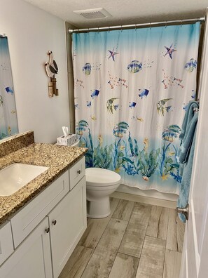 A bathroom with a granite countertop sink, a toilet, and a shower curtain with a marine life design. - Beachfront (Cape Canaveral)