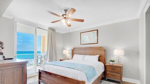 A bedroom with a wooden bed, a ceiling fan, a map on the wall, and a view of the ocean through a sliding door. - 🌊Gulf Views~FREE Beach Svc~Kayak/SUP2~Pools+Splash Pad~BeachFRONT~3BR Azure 407 (Ft. Walton Beach)