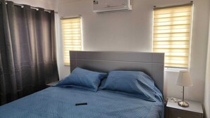 A bedroom with a bed, a nightstand, a lamp, and an air conditioning unit. - Modern Apartment (Juan Dolio)
