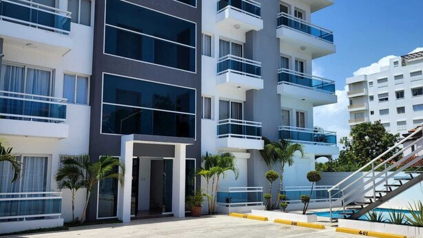 A multi-story hotel with balconies, a swimming pool, and a paved courtyard. - Modern Apartment (Juan Dolio)