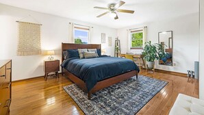 Une chambre à coucher comprenant un lit, un bureau, une chaise, un ventilateur de plafond et un grand miroir.