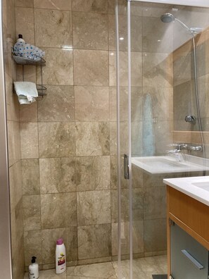 A bathroom with a glass shower enclosure, a sink, and toiletries on the floor.