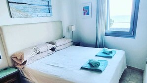 A bedroom with a bed, a ceiling fan, a window with curtains, and artwork on the walls.