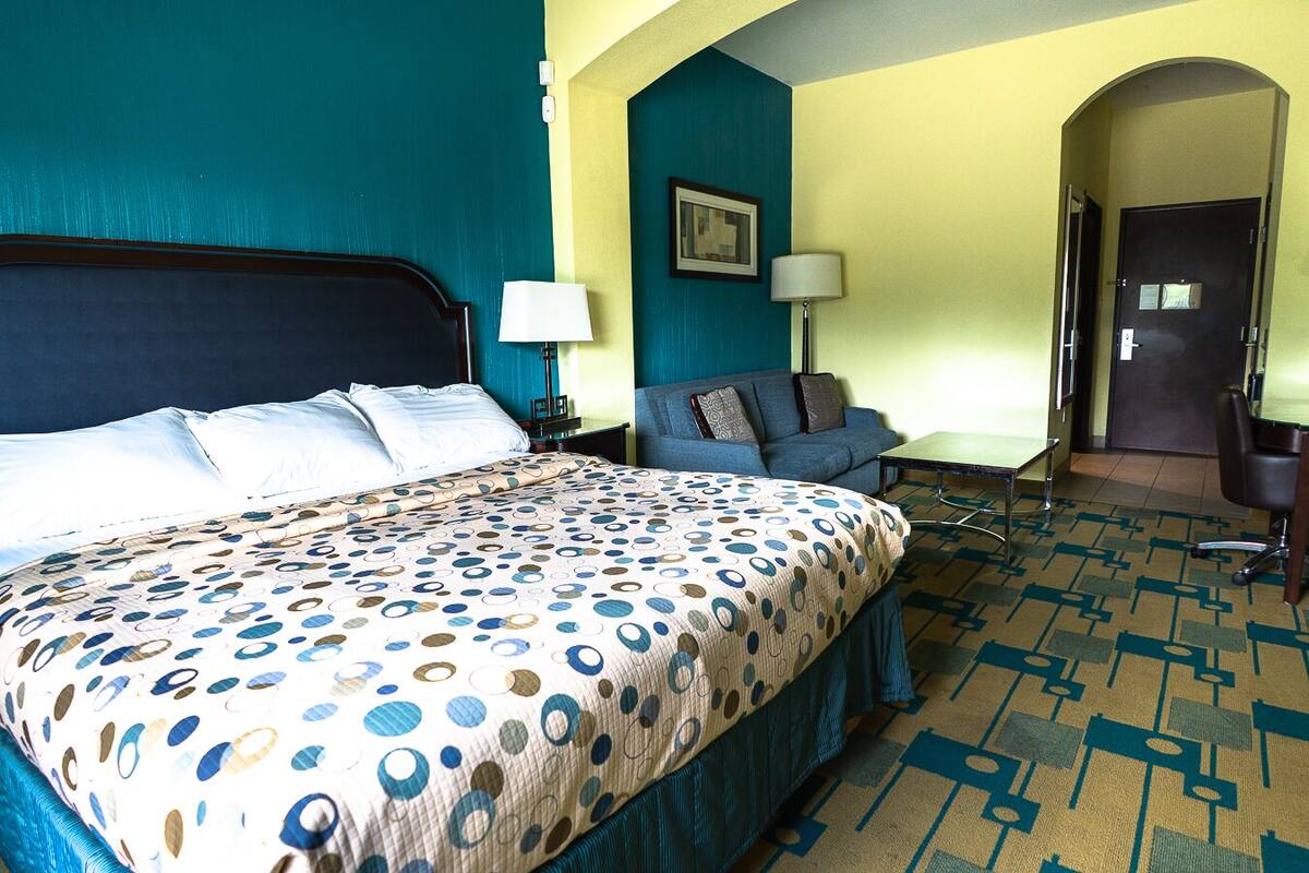 Quarto de hotel com uma cama grande, um sofá, uma escrivaninha e uma porta.