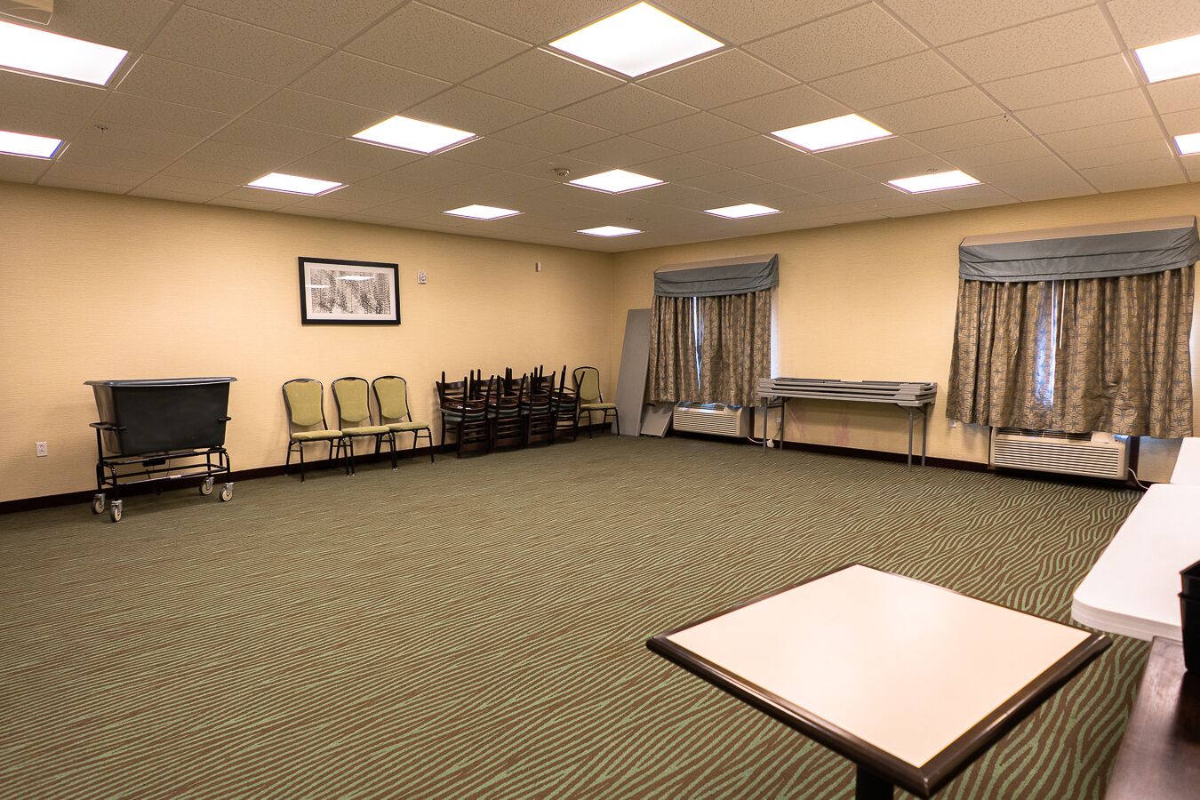 A conference room with a carpeted floor, a projector screen, a table, chairs, and a cart.