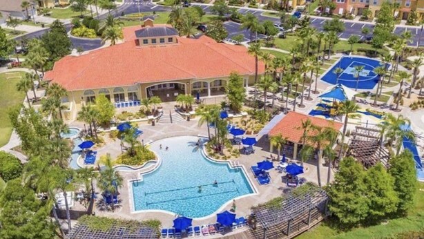 An aerial view of a resort with a central swimming pool, multiple buildings, and surrounding greenery. - Amazing 3/2 Townhome With Lake View at Terra Verde!! (Kissimmee)