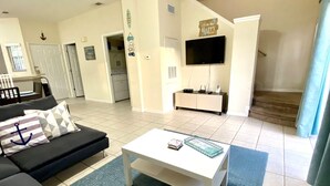 A living room with a sofa, a coffee table, a TV, and a staircase leading to a second floor. - Amazing 3/2 Townhome With Lake View at Terra Verde!! (Kissimmee)