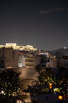 Vista noturna de uma paisagem urbana com edifícios iluminados, incluindo uma estrutura imponente com colunas ao fundo.
