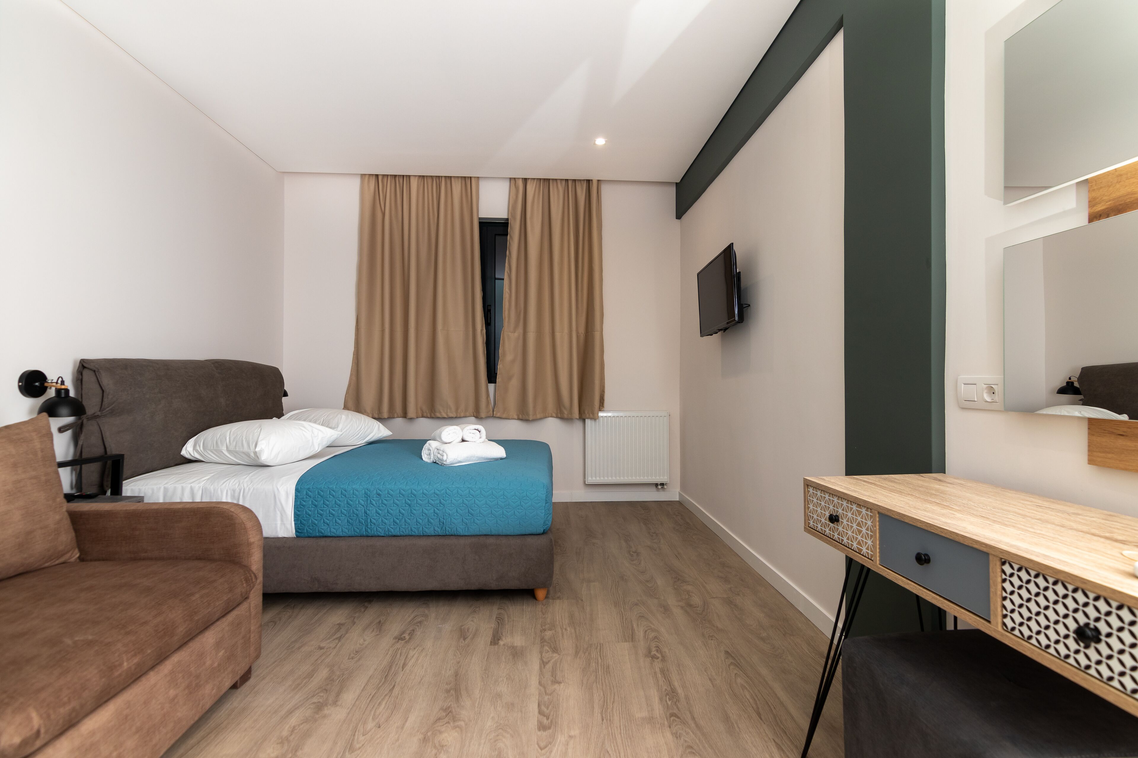 Een moderne hotelkamer met een bed, bureau, stoel, televisie en een raam met gordijnen.