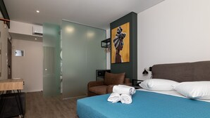 A modern hotel room with a large bed, a desk, a chair, and a painting on the wall. - Dunlin Hotel (Athens)