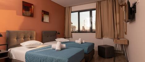 A hotel room with two beds, a desk, a chair, and a TV mounted on the wall.
