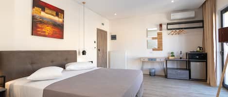 A modern hotel room with a large bed, a desk, and a kitchenette.