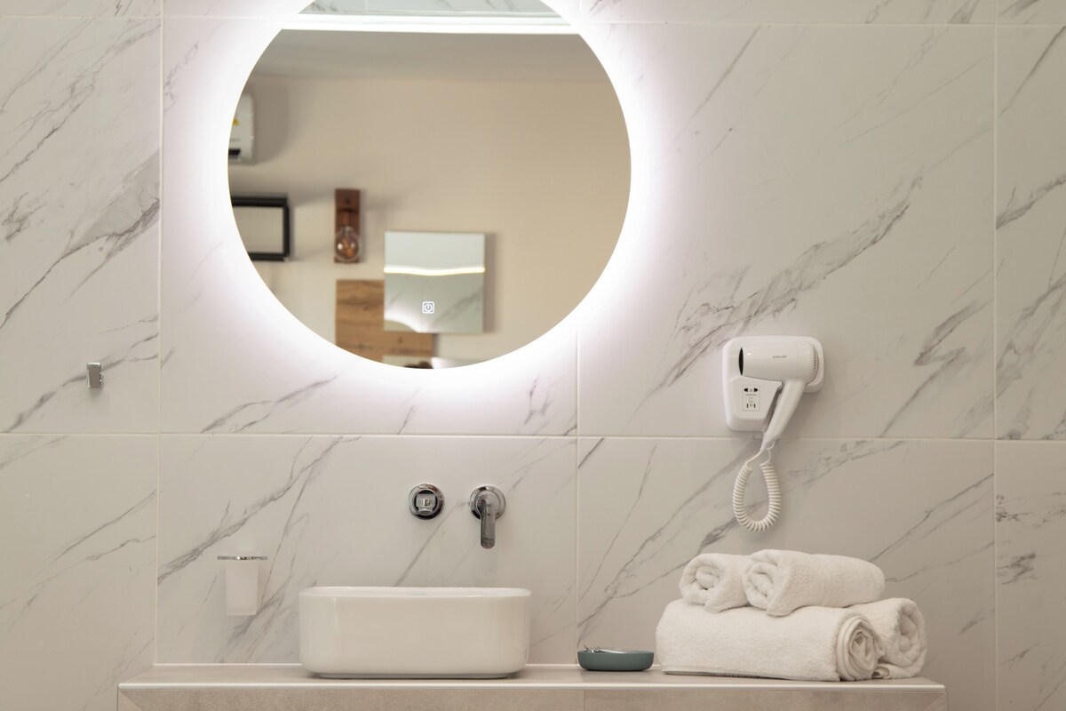 A bathroom with a round mirror, a sink, a towel rack, and a hairdryer.
