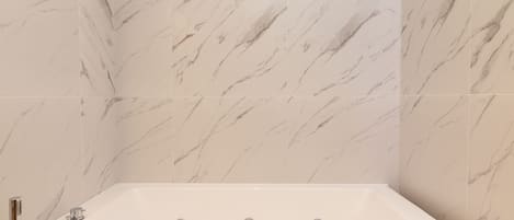Een badkamer met een witte marmeren wand en een badkuip met drie kraanwerk.