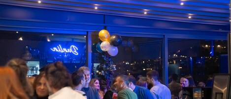 A bar area with a neon sign, balloons, and a city view.