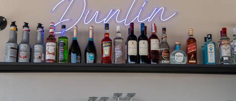 En bar med en neonreklamskylt som visar ordet ”Dublin” och med olika sorters alkoholflaskor och glas.