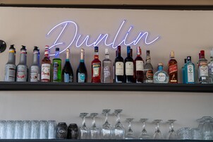 Um bar com um letreiro de neon que diz "Dublin" e vários copos e garrafas de bebidas alcoólicas.