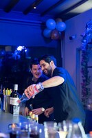 Δύο άτομα σε ένα μπαρ, μπροστά σε μπουκάλια και ποτήρια.