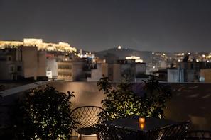 A rooftop terrace with a table and chairs, surrounded by potted plants, overlooking a cityscape at night. - Dunlin Hotel (Athens)