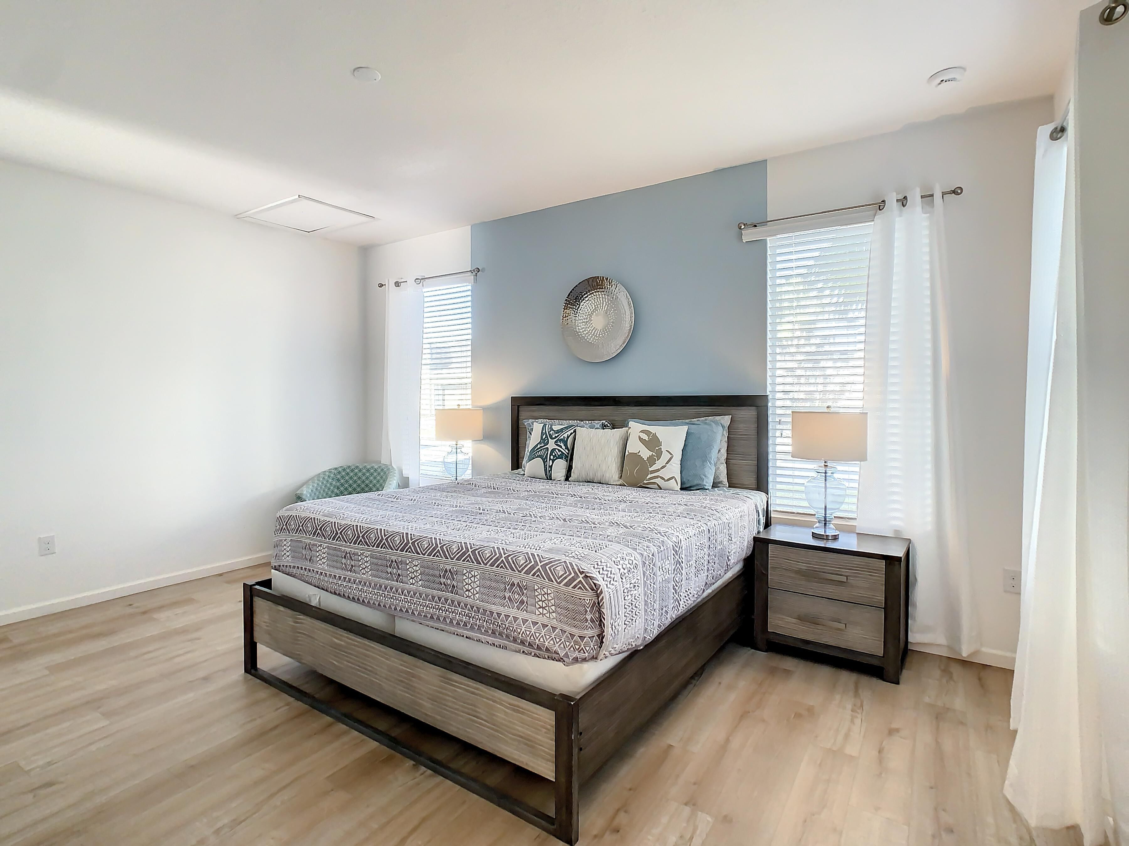 A modern bedroom with a wooden bed, bedside tables, and a large window with curtains.