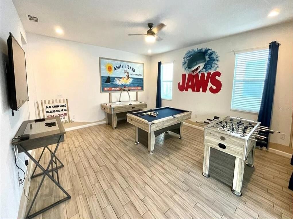 A room with a pool table, foosball table, and a poster of a shark.