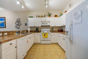 A kitchen with white cabinets, a microwave, a stove, and a refrigerator. There is a clock on the wall and a plant on the counter. - Huge Screened Patio That Overlooks Lake Buck, Near Famous Attractions!! (Kissimmee)