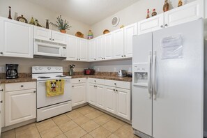 A kitchen with white cabinets, a microwave, stove, and a refrigerator. There are various kitchen appliances and items on the countertops. - Huge Screened Patio That Overlooks Lake Buck, Near Famous Attractions!! (Kissimmee)