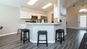 A modern kitchen with white cabinets, a central island with stools, and a microwave. - Private Pool, Close to Disney!!! (Kissimmee)