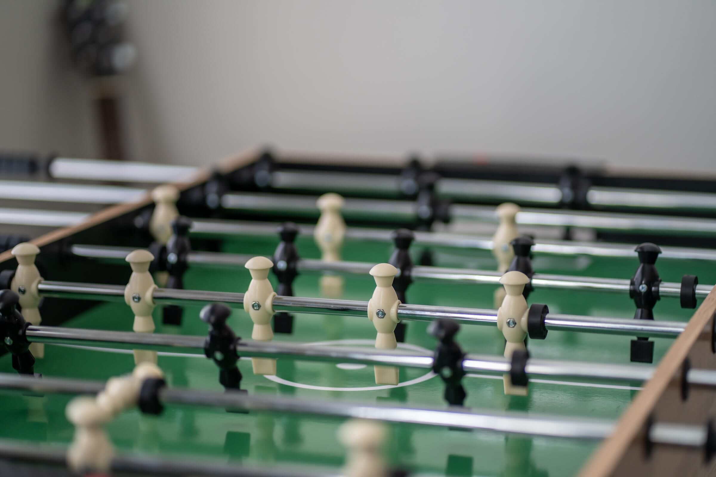 Ein Detailbild eines Kicker-Tisches mit zwei Mannschaften aus Figuren, eine in Weiß und die andere in Schwarz, auf einer grünen Spielfläche.