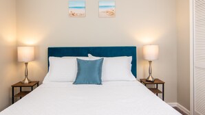 A neatly made bed with a blue headboard, two bedside lamps, and two wall-mounted pictures of beaches. - Private Pool, Close to Disney!!! (Kissimmee)