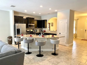 A modern kitchen with a central island, bar stools, and a dining area.