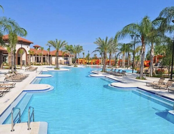 Relax by the resort's clear blue pool surrounded by palm trees and lounge chairs, set amidst a Mediterranean-style courtyard with stucco walls and terracotta roof tiles.