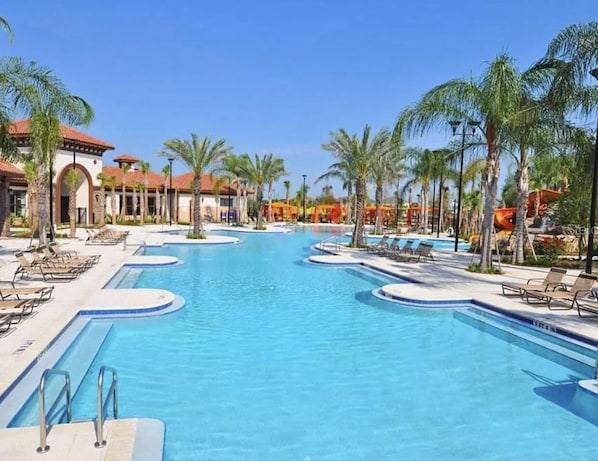 Relax by the resort's clear blue pool surrounded by palm trees and lounge chairs, set amidst a Mediterranean-style courtyard with stucco walls and terracotta roof tiles.
