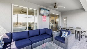 A covered outdoor seating area with a sofa and chairs, a television, and a ceiling fan. - Amazing 5/6 Vacation Home at Windsor Island Resort!!! (Davenport)