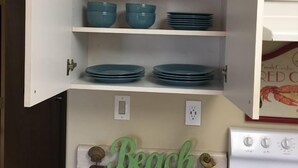 A kitchen with a cabinet containing blue dishes and a 'RELAX' sign above it. - Sea Breeze Cottage - Venture Out Unit 066 (Cudjoe Key)
