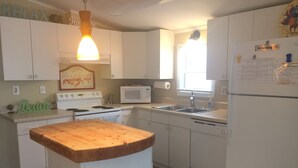 A kitchen with white cabinets, a wooden countertop, a stove, a microwave, a sink, and a refrigerator. - Sea Breeze Cottage - Venture Out Unit 066 (Cudjoe Key)