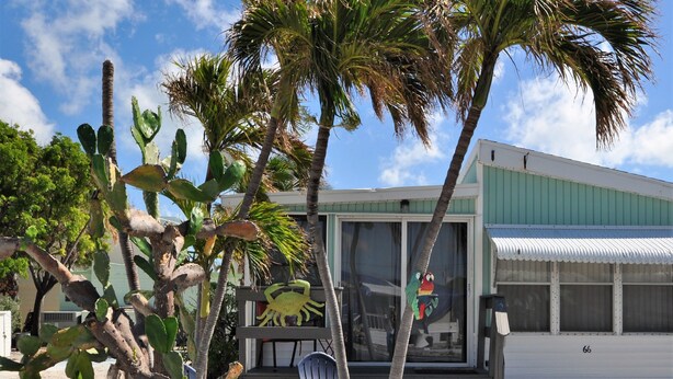 A small, single-story building with a green roof and white walls, featuring a large window and a door. - Sea Breeze Cottage - Venture Out Unit 066 (Cudjoe Key)
