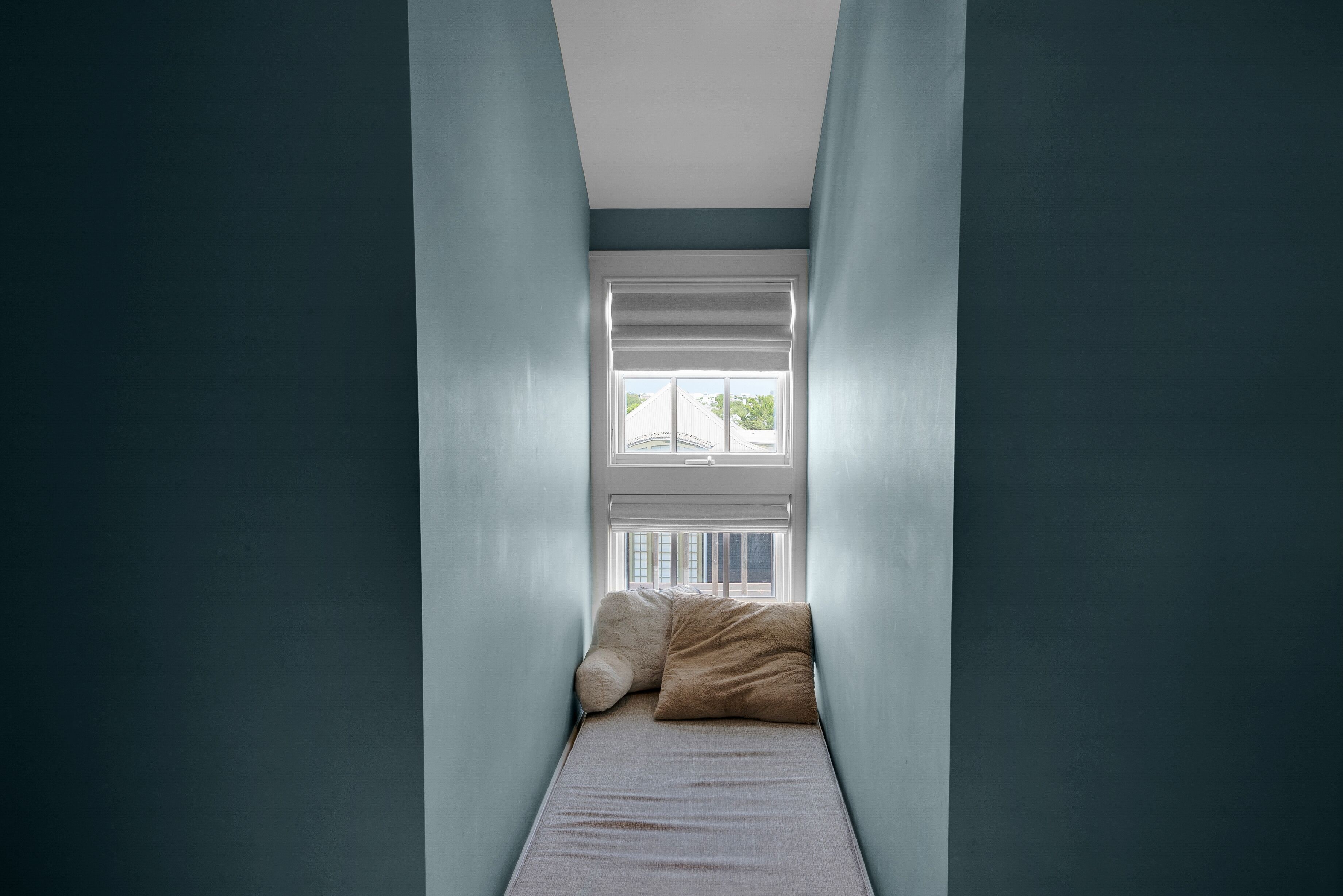 A narrow room with a window, a bed, and two pillows.