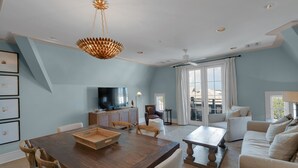 A spacious living room with a wooden dining table, a large flat-screen TV, and a ceiling fan.