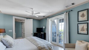 A bedroom with a bed, a dresser, a ceiling fan, and a balcony with a view.