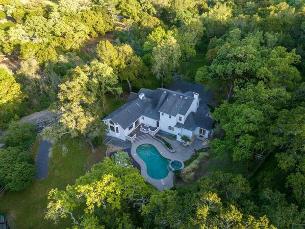 A large house surrounded by dense trees, with a swimming pool and a driveway.