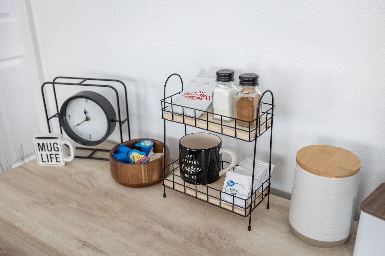 Una encimera de cocina con una cafetera, una taza, saleros y pimenteros, un reloj y una taza con el texto 'Mug Life'.