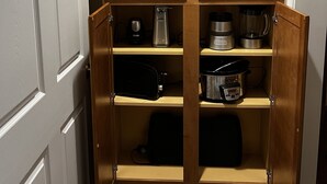Eine Küche mit Holzschränken, einer Kaffeemaschine, einem Toaster und einem Slow Cooker auf den Regalen.