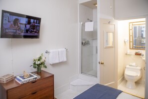 Een badkamer met een douche, toilet en een tv aan de muur die een nieuwsprogramma vertoont.