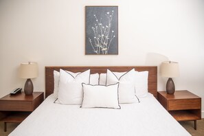 A neatly made bed with white bedding and multiple pillows, flanked by two bedside tables with lamps and a framed artwork above. - Standard King Room with Ensuite Bathroom (San Francisco)