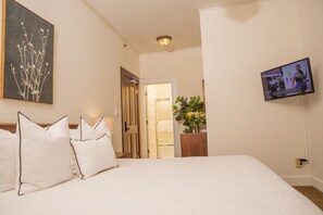 A hotel room with a bed, pillows, a television, a painting, and a door leading to a bathroom. - Standard King Room with Ensuite Bathroom (San Francisco)