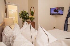 A hotel room with a bed, a TV on the wall, a mirror, and a plant.