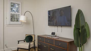 A room with a wooden cabinet, a chair, a large plant, and a TV on the wall.